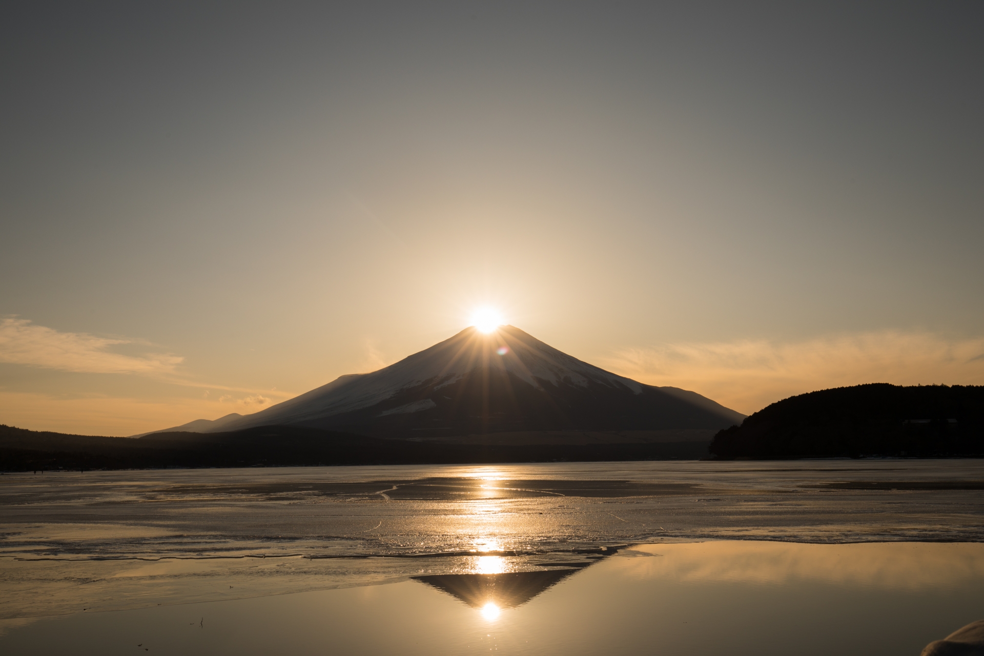 Low sunlight above Mount Fuji, reflected across the water.