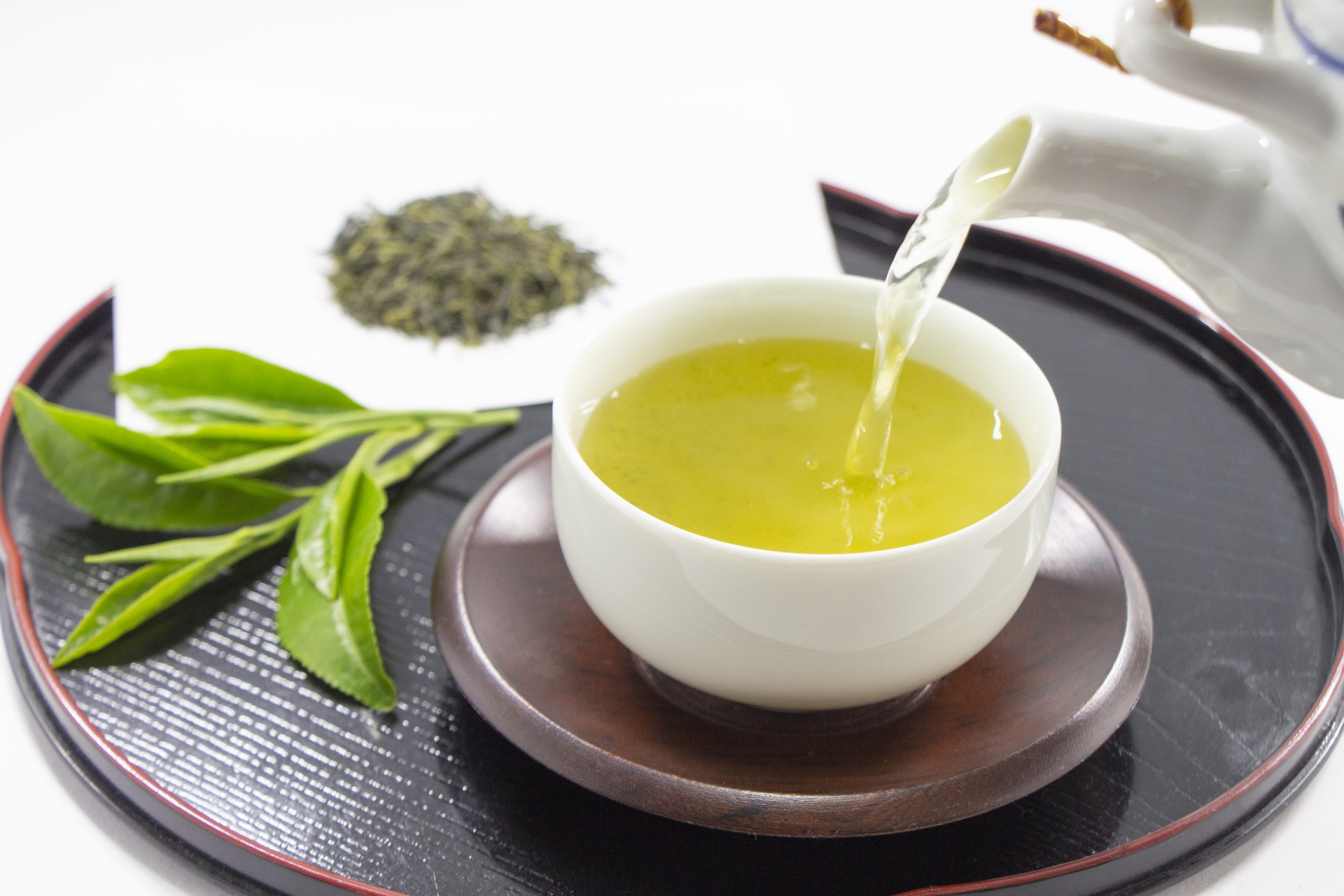 Sencha being poured from a white teapot into a cup on a dark tray.