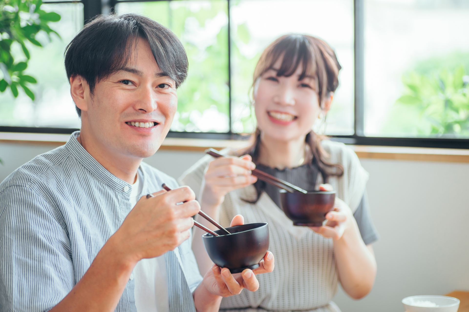 Two people holding lacquer bowls and using chopsticks at a table.