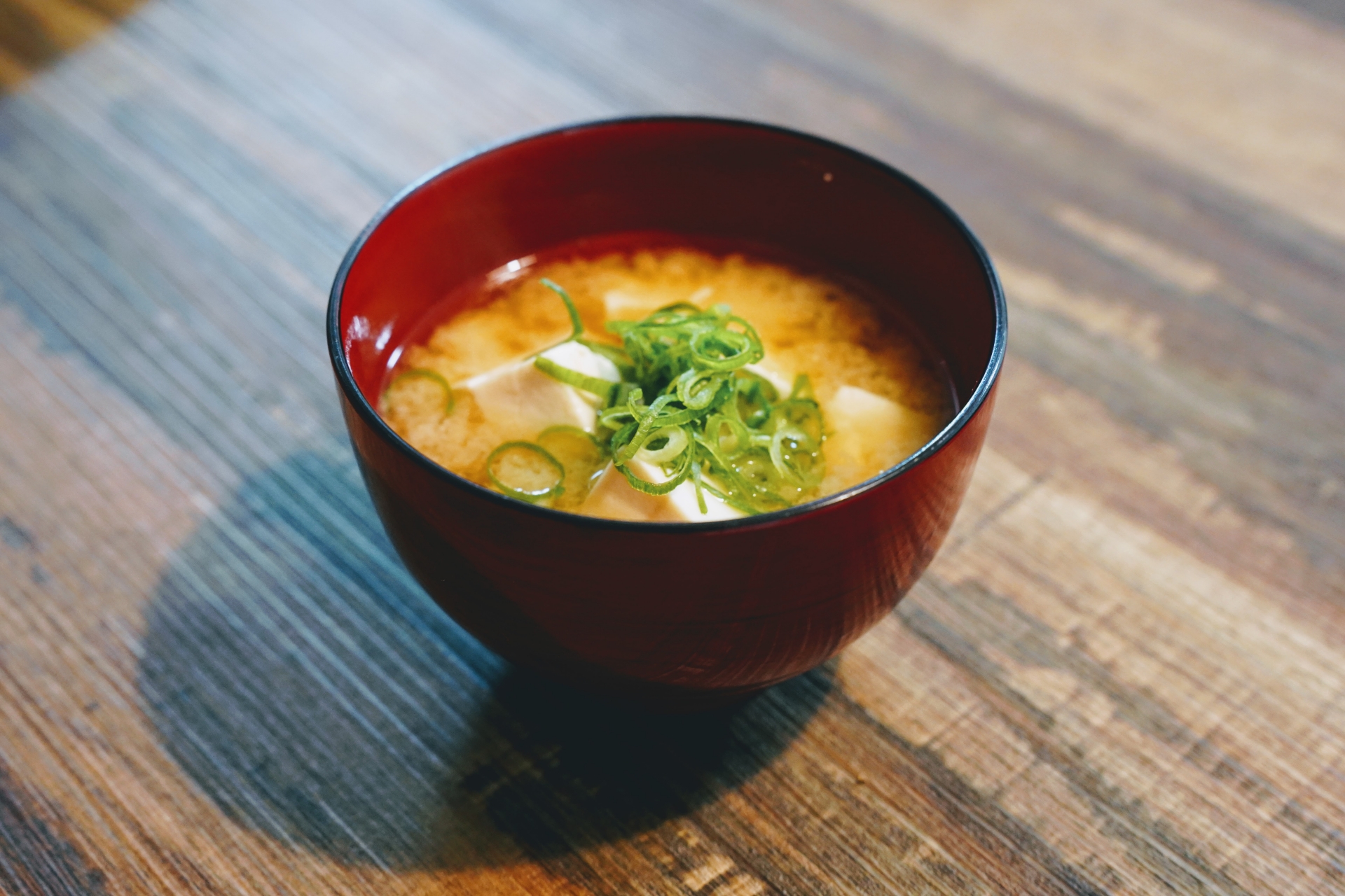 Miso soup served in a red and dark lacquer bowl.