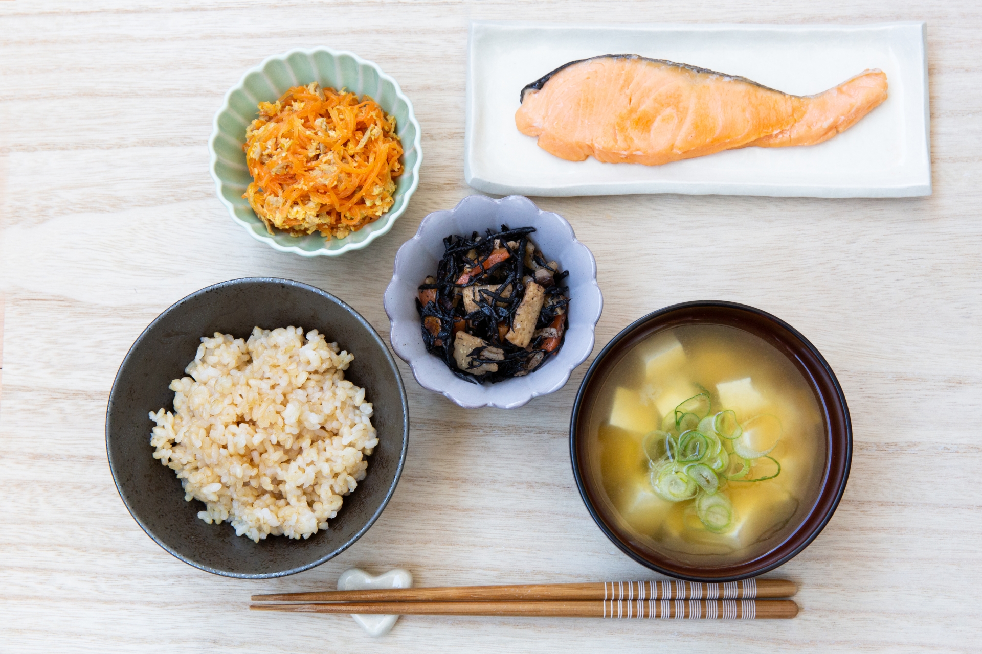 A meal of rice, miso soup, salmon and two vegetable dishes served in varied vessels.