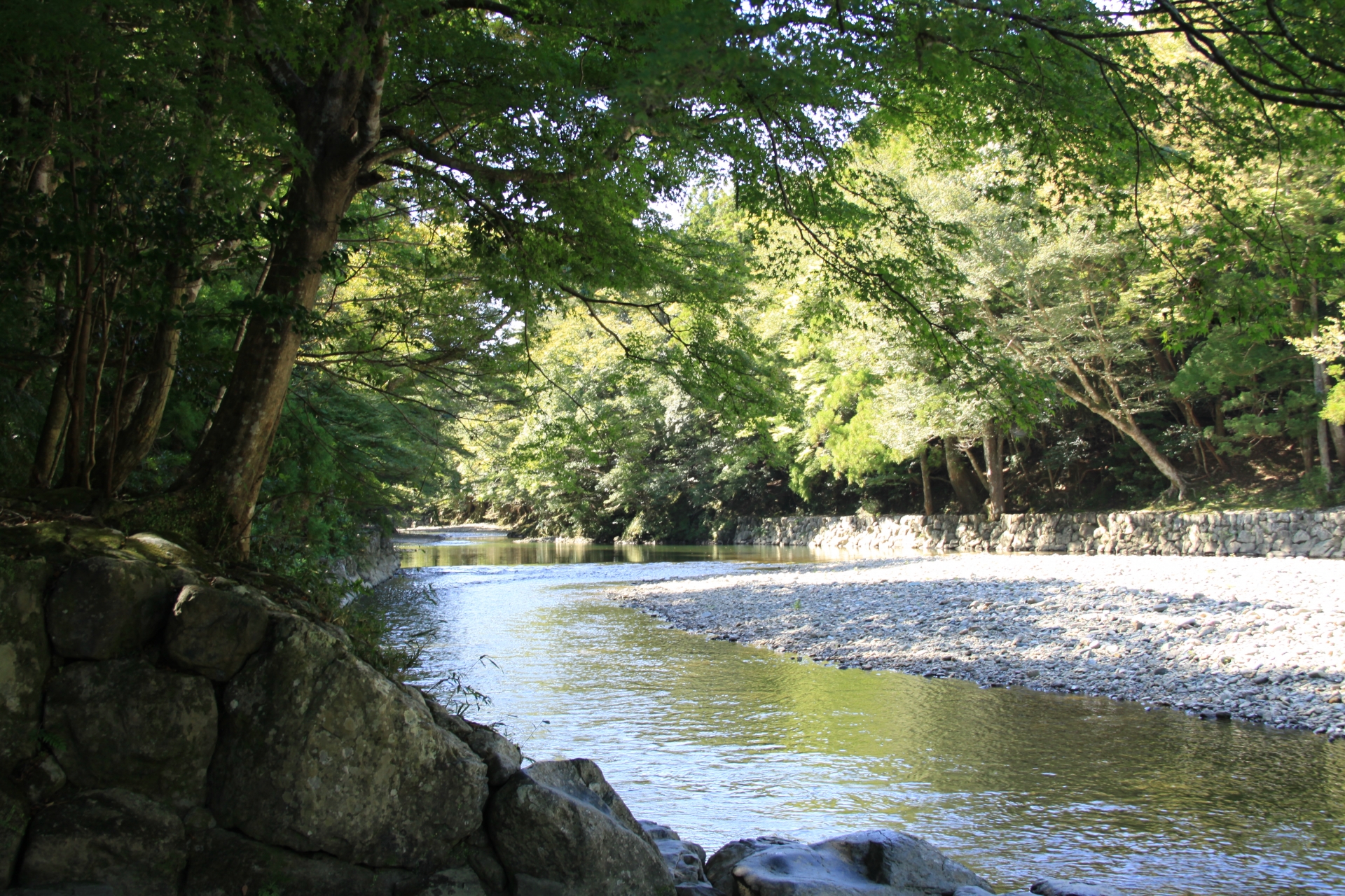 The Isuzugawa river beneath green trees, with stones along the riverbank.