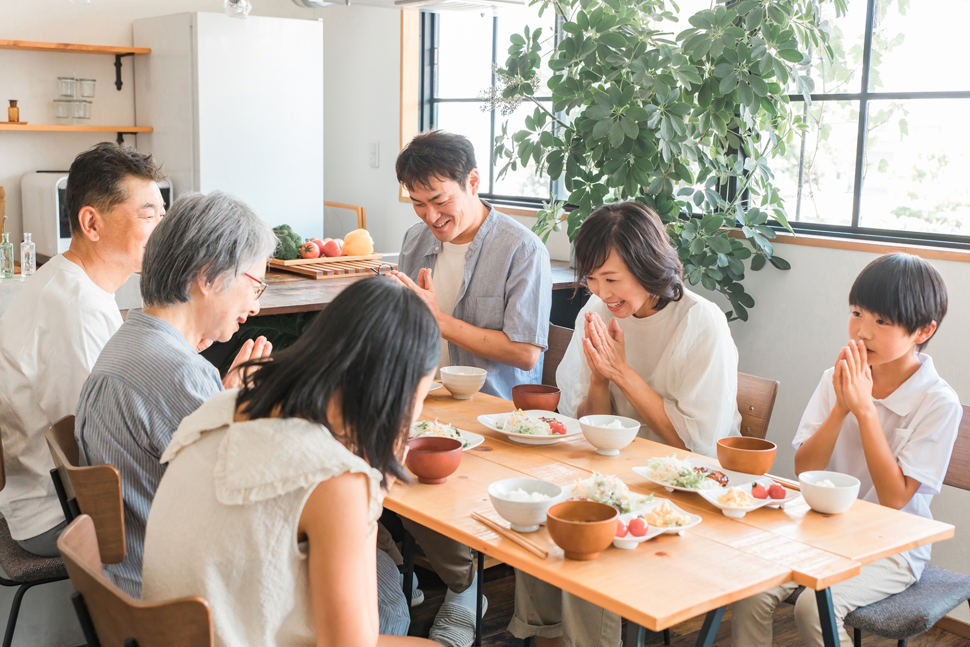 A family gathered around a Japanese meal with their hands together before eating.