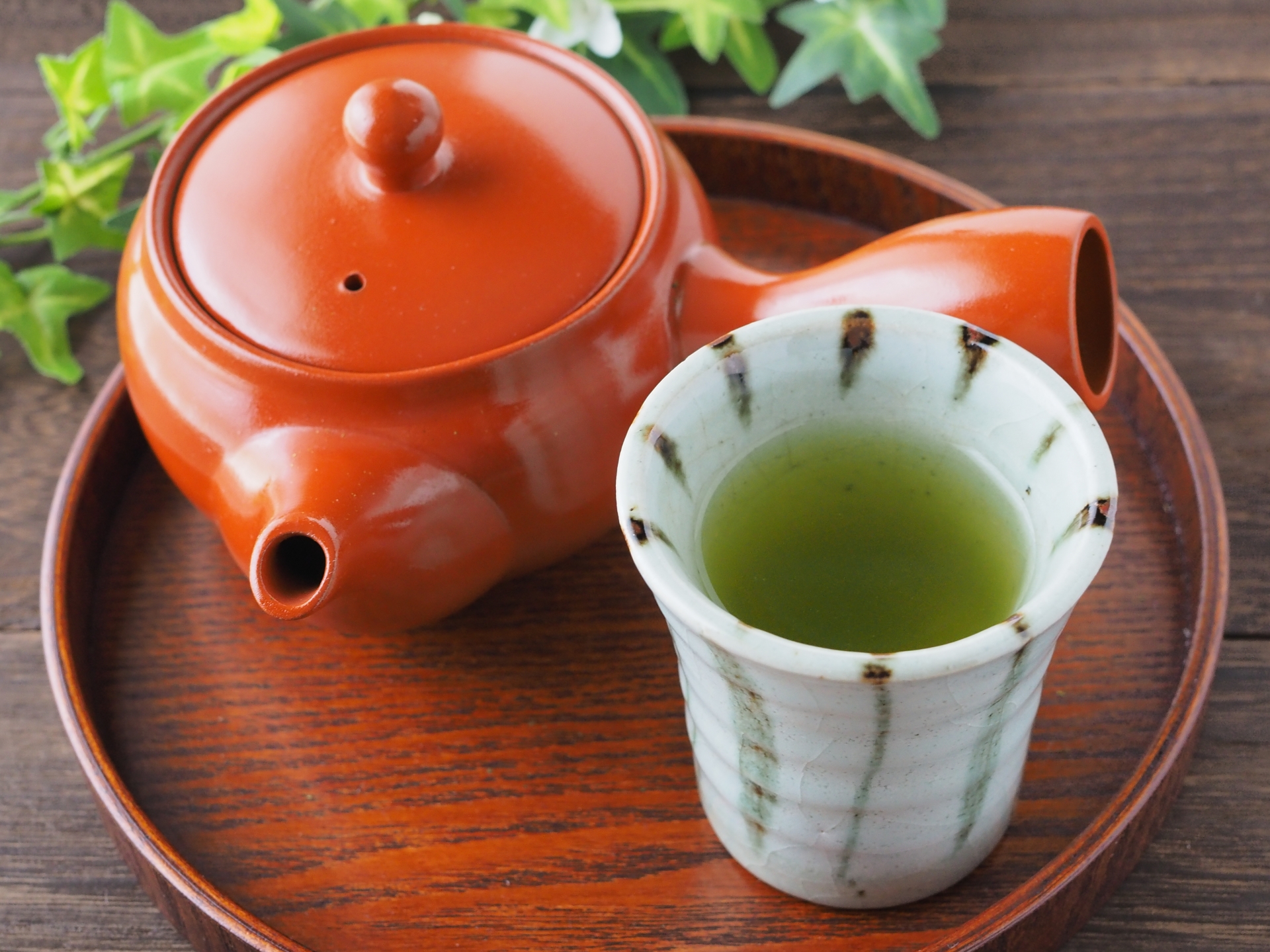 A cup of sencha beside a red side-handled kyusu.