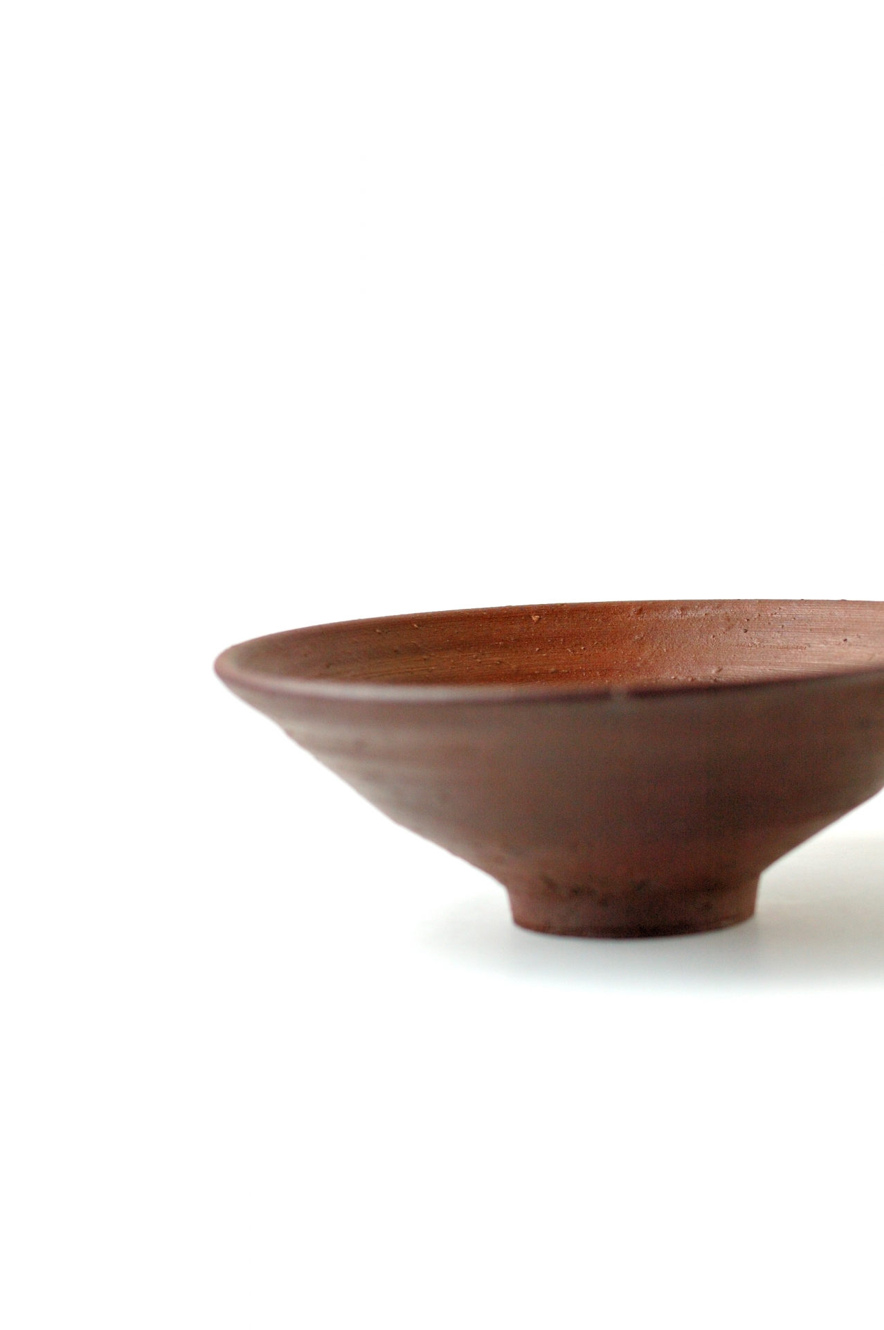 A reddish-brown Bizen pottery bowl showing the unglazed clay and raised foot.