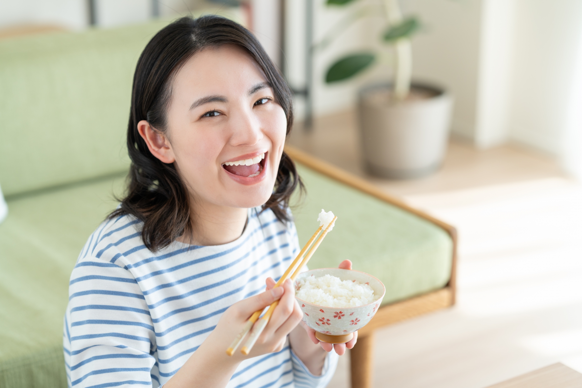 A woman holding a rice bowl and eating with chopsticks.