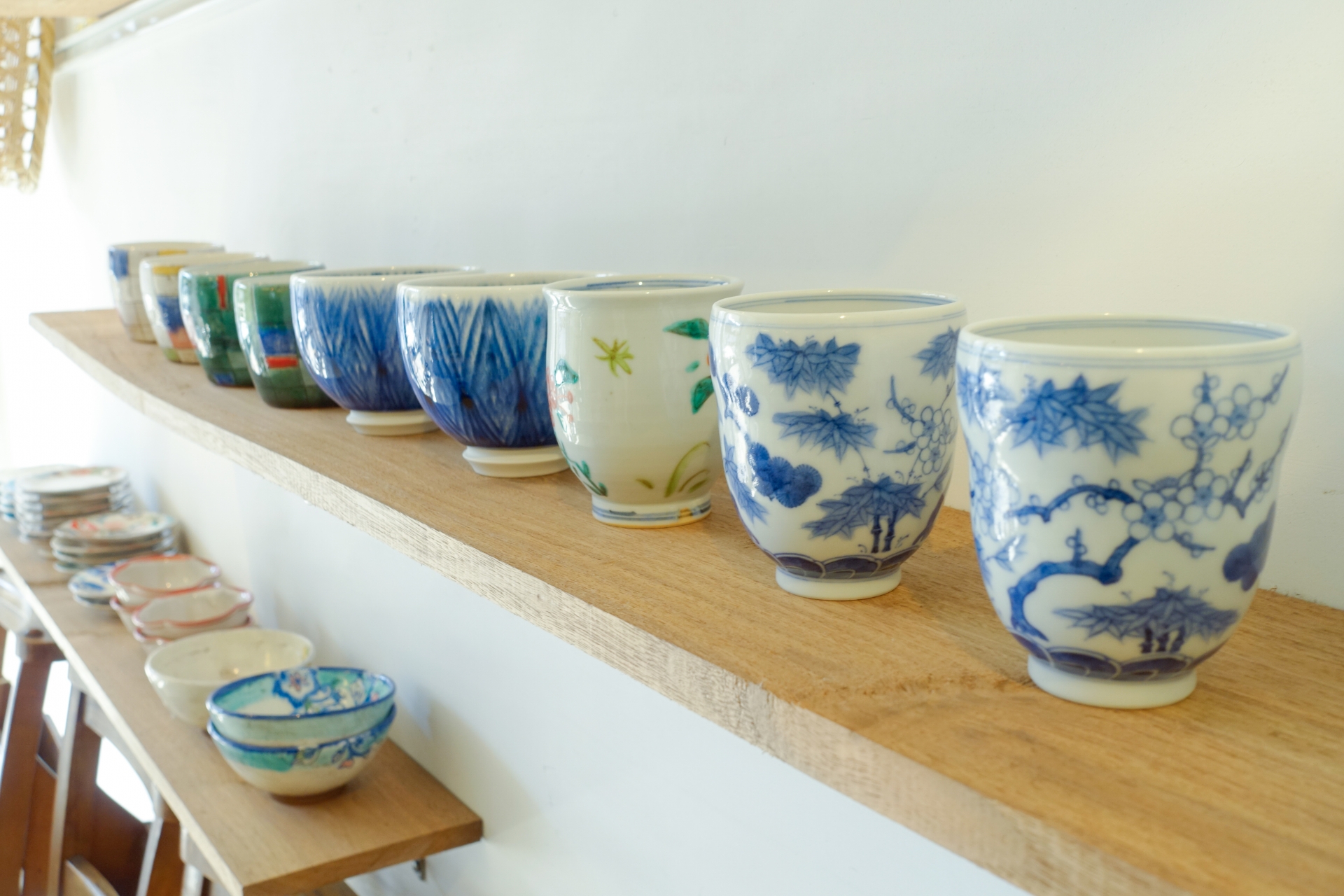 Japanese tea cups with varied shapes and decoration displayed on wooden shelves.