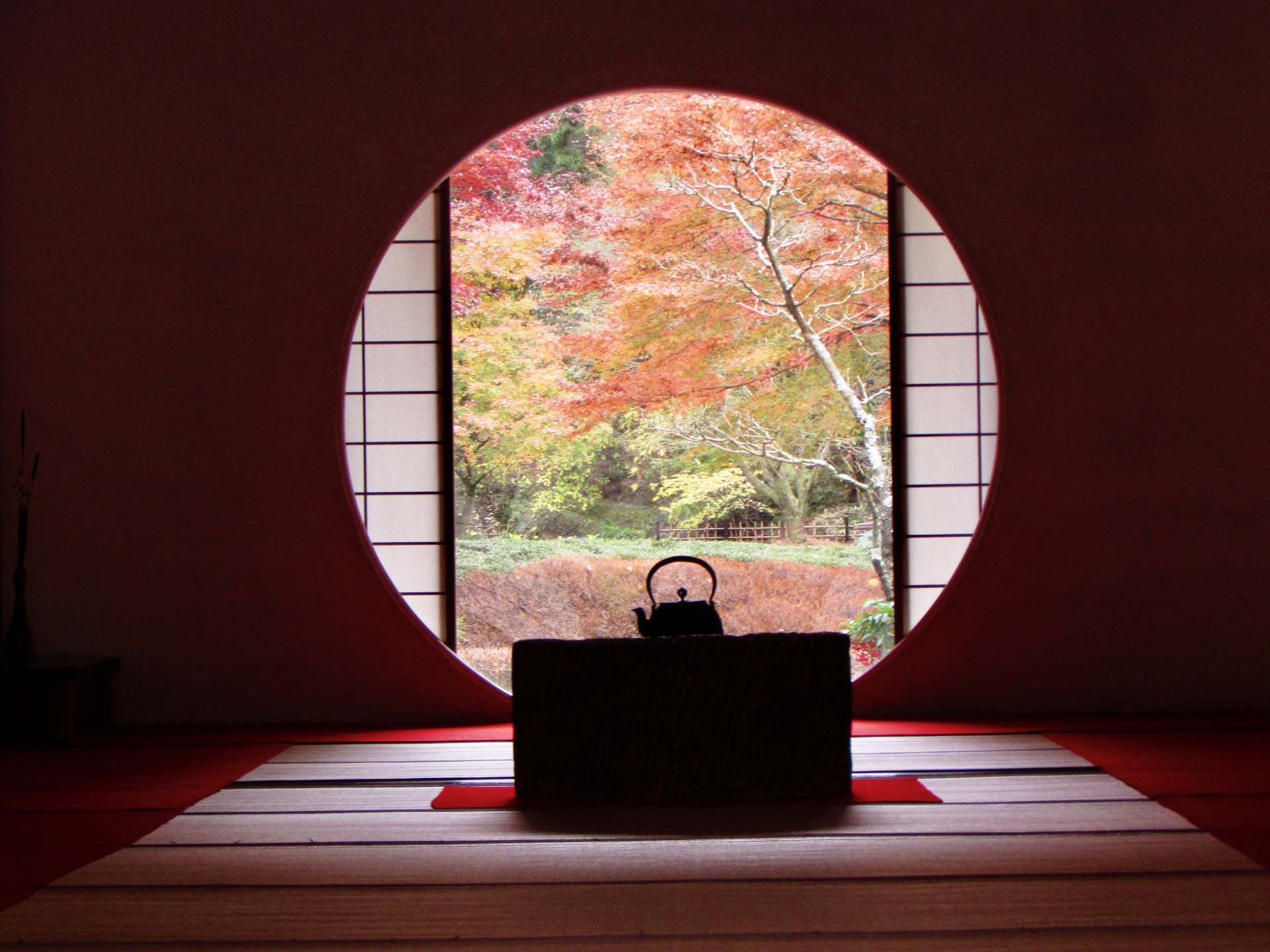Dark Japanese interior framing an autumn garden through a circular opening.