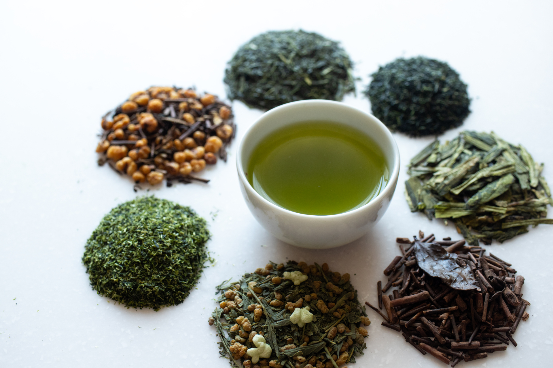 A cup of green tea surrounded by several different Japanese tea leaves and blends.