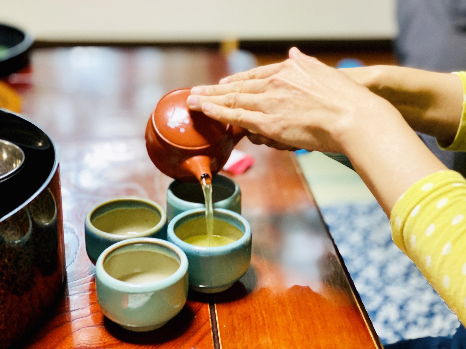 Tea being poured from a side-handled kyusu while the other hand steadies the lid.