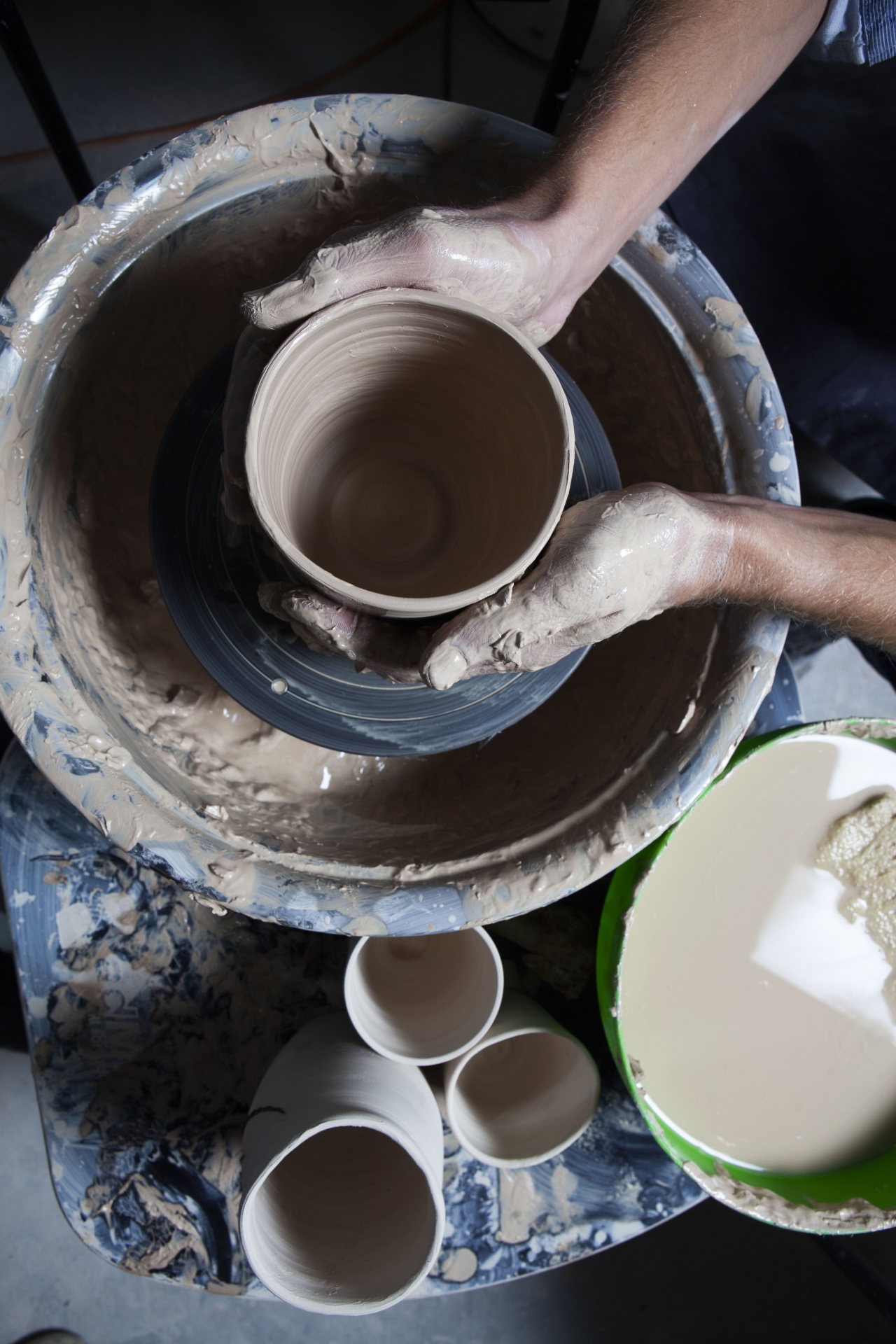 Hands shaping a clay vessel on a pottery wheel.