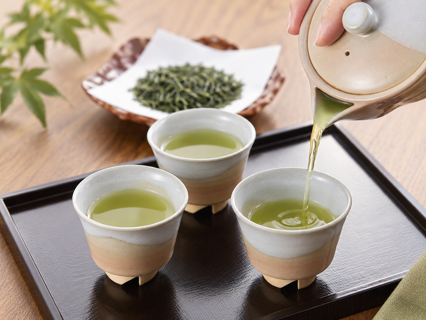 Japanese green tea being poured from a kyusu into small cups.
